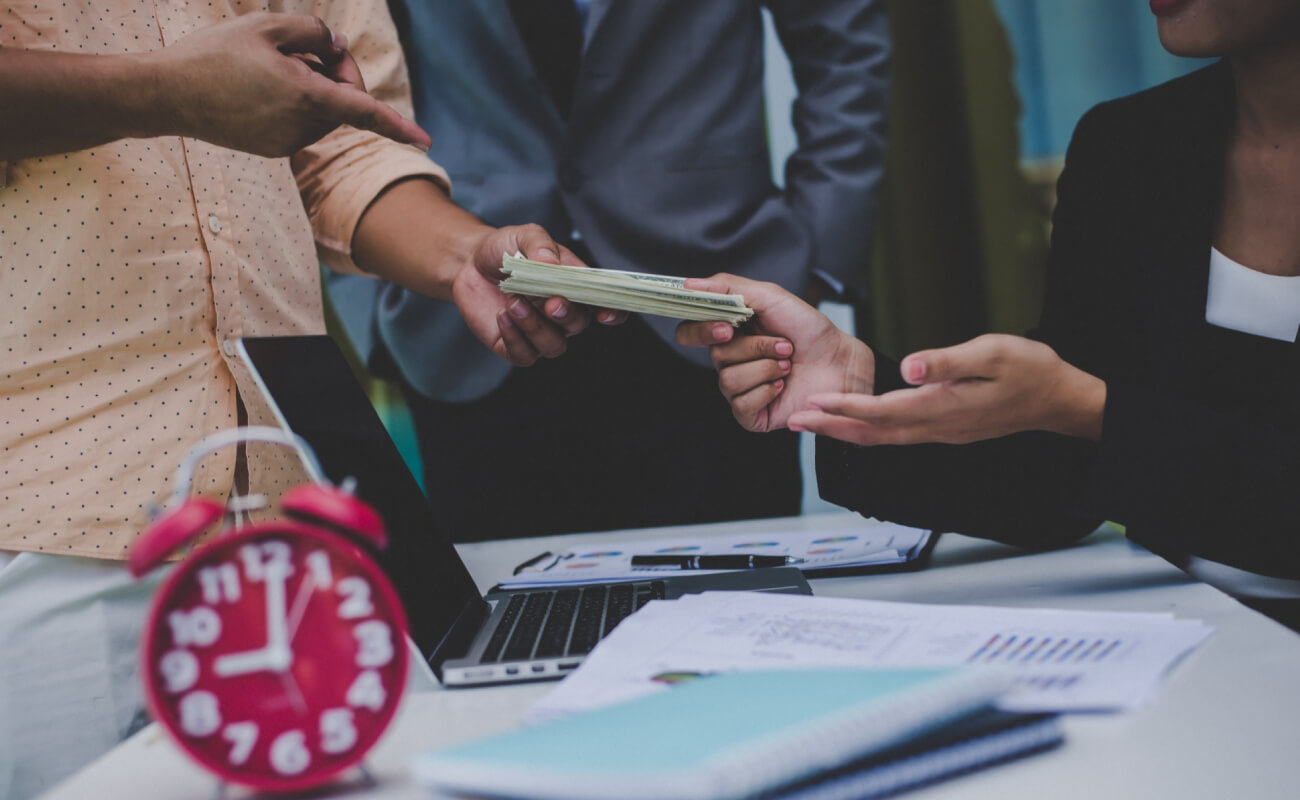 Business professionals exchanging cash during a financial consultation, with a laptop and documents on the table, symbolizing business funding solutions.