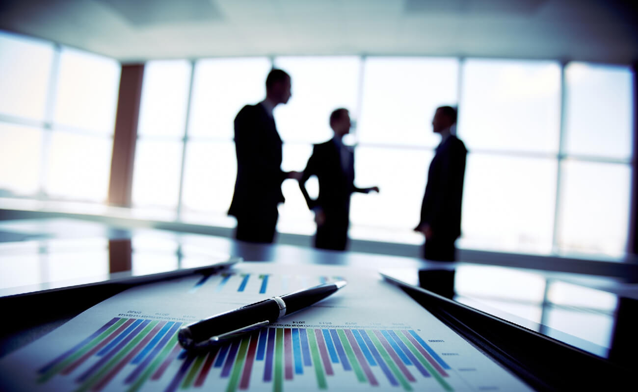 Business professionals discussing financial strategies, with a focus on a report featuring colorful bar graphs and a pen in the foreground, emphasizing EJN Financial's consultancy services.