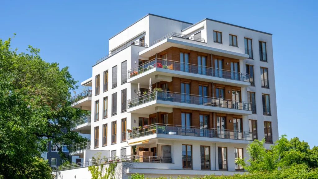 Modern multifamily residential building with balconies and large windows, surrounded by greenery, representing investment opportunities in real estate financing.
