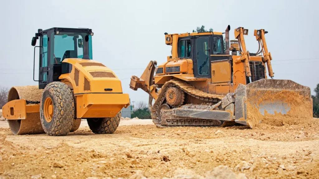 Heavy construction equipment, including a roller and a bulldozer, on a sandy worksite, symbolizing equipment financing options for businesses.