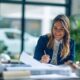 in a sleek, modern office adorned in navy, gold, and white, a confident female financial advisor engages with diverse clients—real estate investors and small business owners—surrounded by property blueprints, construction helmets, and financial documents, all underscored by the elegant phrase ‘think outside the bank’.