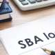 A photo of an office table with a paper written SBA loan with calculator, notebook and pen