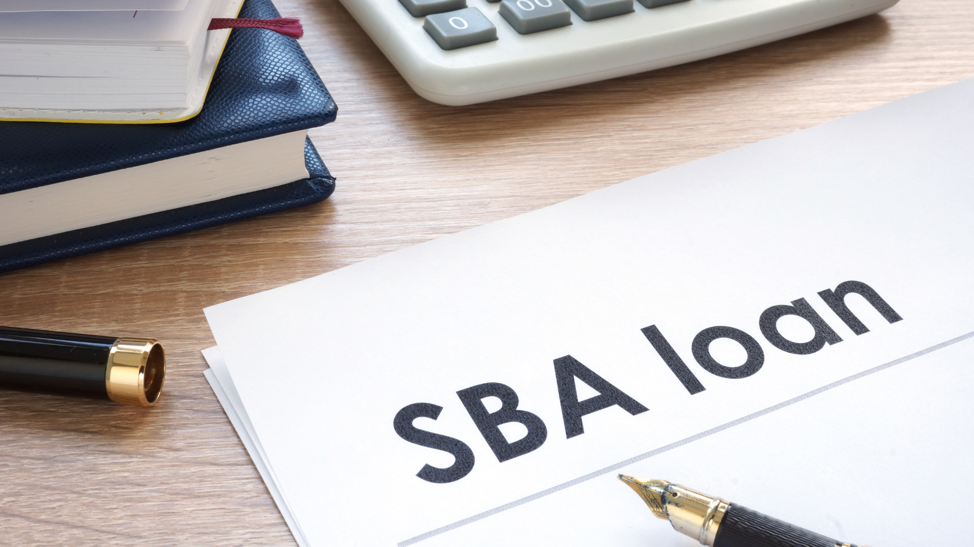 A photo of an office table with a paper written SBA loan with calculator, notebook and pen
