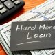 Hard money mortgage lenders—stack of $100 bills, calculator, and handwritten loan note on wooden surface