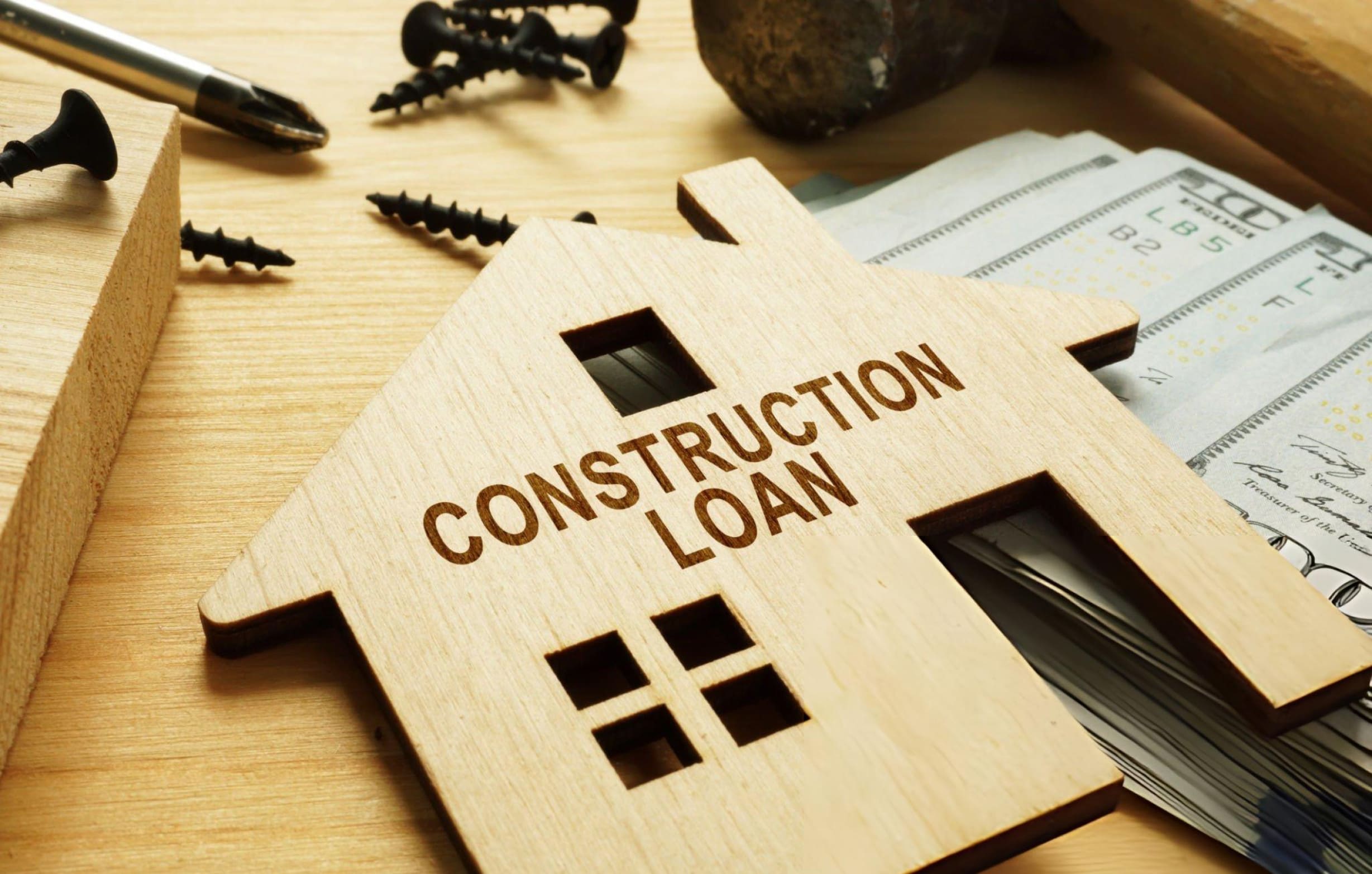 Construction loan lenders near me—wooden house cutout with tools and cash on work surface.