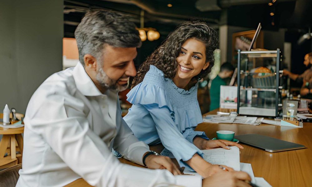 Florida commercial loan discussion—small business partners collaborating in café with laptop and notebook