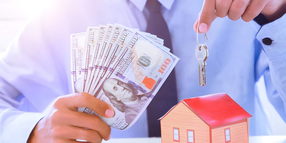 Fix and flip loans near me—businessperson holding cash and house keys beside model home on table.